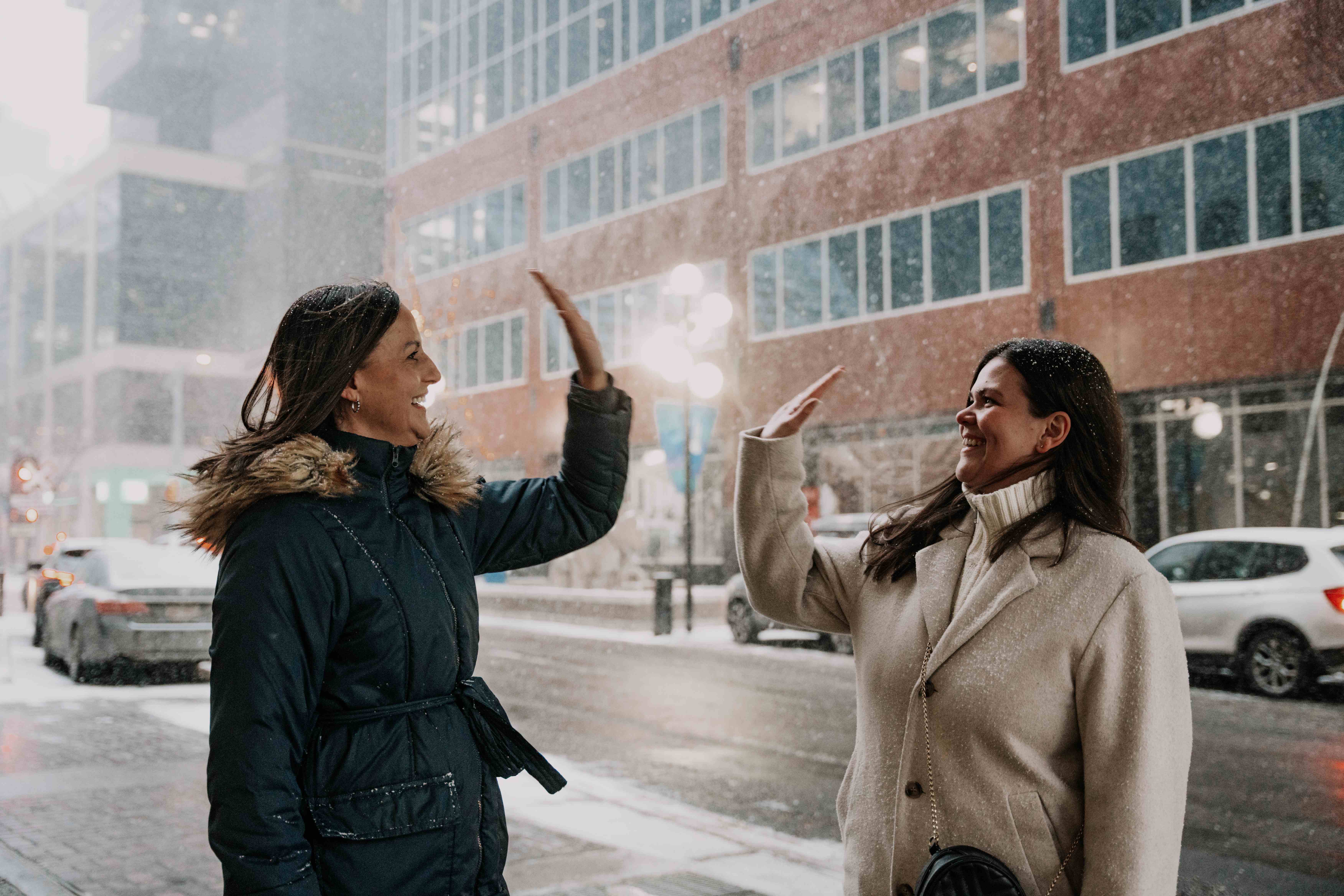 Two women high-fiving on a snowy Canadian city street
